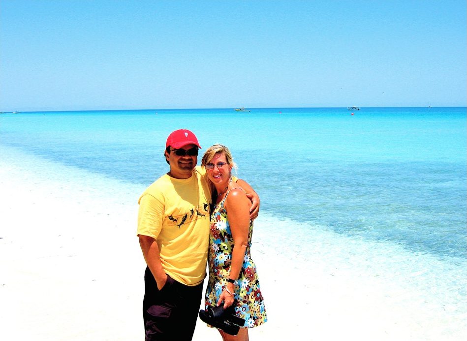 Gil and his wife on a white-sand beach with turquoise water